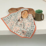 Sienna Earth Block-Printed Kitchen Towel with florals holds bread beside a board and green mug.