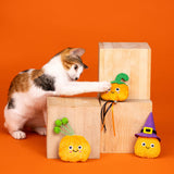 A cat plays with the Witch of the Patch Cat Toy Set—plush pumpkins and a witch hat—on an orange background.