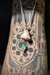 The Australian White Opal Necklace, featuring a sterling silver opal pendant with a small bone charm and green opal detail, rests on an arm adorned with detailed black geometric and ornamental tattoos.