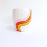 The Cali Rainbow Handmade Pot is a white ceramic vessel with pink, orange, and yellow wavy stripes—ideal for stylish home decor or displaying small succulents on a plain white background.