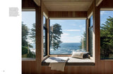 A window seat with pillows overlooks ocean and trees.