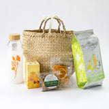 The California Welcome Gift Basket with Custom Logo Water Bottle includes a ribbon-handle straw basket, floral logo water bottle, dried mango, dried orange slices, roasted almonds, and sea salt & olive oil chips—ideal California treats for gifting.