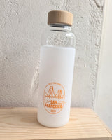 The California Welcome Gift Basket includes a frosted glass custom logo water bottle with a wooden cap featuring orange San Francisco bridge graphics and "Destinations San Francisco 2024"—ideal as a California souvenir or gift.