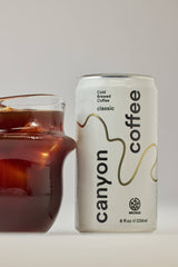 A glass of iced Canyon Cold Brew Coffee sits beside a ready-to-drink Canyon Cold Brew Coffee can.