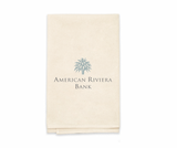 The Custom Logo Kitchen Towel is a folded beige cloth made from 100% natural cotton, featuring a blue palm tree logo with "American Riviera Bank" printed beneath.
