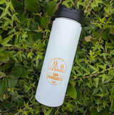 The Custom Logo Sequoia Stainless Tumbler, in white stainless steel with a black lid, sits on green leaves. It displays an orange bridge outline and the custom Destinations San Francisco 2024 logo text.