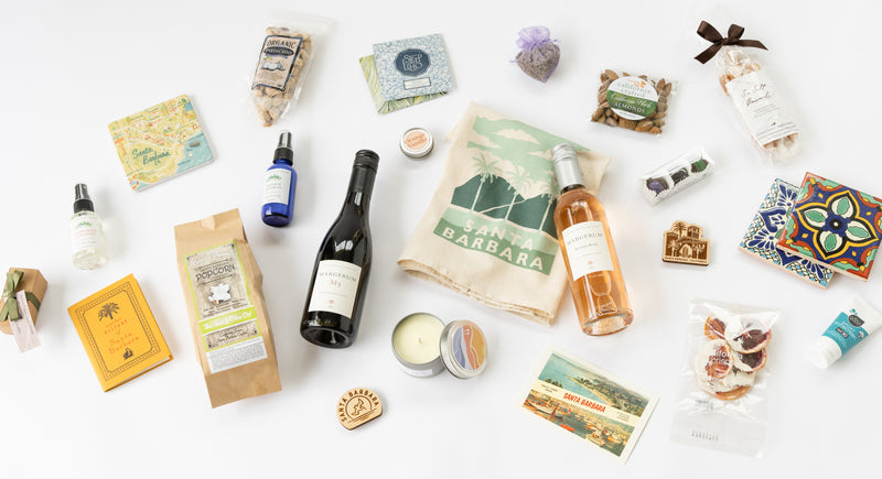santa barbara products displayed on a white background including coasters, chocolate, treats, lip balm, kitchen towel, wine, books and more. 