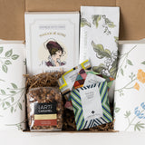Open Verdon Coffee and Tea Gift Box with SBCO whole bean coffee, three Art of Tea sachets, Makabi and Sons Verdon shortbread cookies, and Art of Caramel Mayan chili chocolate popcorn nestled in kraft paper inside a floral-patterned mailer box