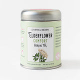 A tin of Elderflower Comfort Herbal Tea featuring a botanical illustration on a light green label.
