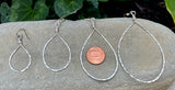 four sizes of Gold Pear Shaped Hammered Hoops beside a penny for scale, displayed on a stone surface.