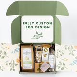 Open Happy SB Treats Gift Box with Custom Logo, featuring a floral interior, filled with assorted Santa Barbara snacks, organic popcorn, a soap bar, a small box, and other packaged treats on a white background.