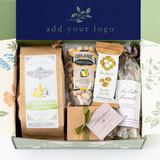 The Happy SB Treats Gift Box with Custom Logo includes Santa Barbara snacks—organic popcorn, pistachios, a macadamia seed & nut bar, and lavender sea salt caramels—in a brown box featuring your custom logo on the lid.