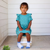Young child in a teal dress sits on stacked books, wearing Kids Socks Gray Bicycles and looking forward.