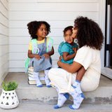 A mother hugs one child while another, both in Kids Socks Gray Bicycles, sit on the porch with matching socks.