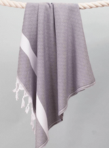 A Custom Logo Beach & Bath Towel with gray and white stripes and tassels hangs over a thick rope.