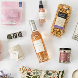 Gift items on white: Margerum Santa Barbara Rosé, popcorn, tea, chocolates, soap, spray, and a floral pouch.