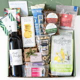 The Moret Savor California Gift Box features California wine, crackers, Meyer Lemon Shortbread Cookies, nuts, chocolate, tea, jam, and gourmet snacks—beautifully arranged on white paper in a green box with positive words.
