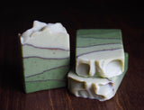 Three bars of Ojai Trails Ojai Botanika Soap, green and cream marbled, rest on a wooden surface.