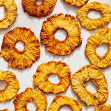 Organic Dried Pineapple rings, golden-brown and textured, are arranged on a white surface—an eco-friendly snack ideal for those who appreciate delicious, sustainable treats.