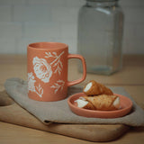 Poppy Ceramic Mug with white floral design and two cannoli on matching plate; microwave & dishwasher safe.