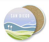 The San Diego Vistas Coaster is a round ceramic stone coaster featuring an abstract landscape of hills, palm trees, birds, and "San Diego" at the top. Its cork underside is partially visible.