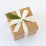 Brown gift box with a white ribbon and greenery on a white background