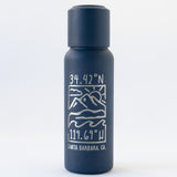The Santa Barbara Coordinates Insulated Bottle & Cup Set features a navy-blue stainless steel bottle with white line art of mountains, ocean waves, and 34.42°N 119.69°W above Santa Barbara, CA. Copper vacuum insulation ensures lasting temperature control.
