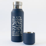 The Santa Barbara Coordinates Insulated Bottle & Cup Set is a navy blue stainless steel thermal bottle with copper vacuum insulation, a detachable cup, and features mountain and wave graphics, coordinates (34.42°N, 119.69°W), and "Santa Barbara, CA.