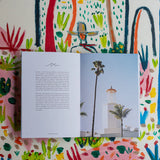 The open Santa Barbara Guide Book rests on a colorful floral surface, showing a lighthouse and palm trees inside.