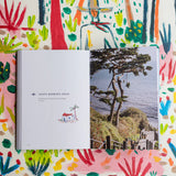 An open Santa Barbara Guide Book on a colorful surface; one page reads "Santa Barbara Gems," the other shows a photo of wooden steps leading to a beach.
