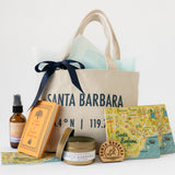 A gift set featuring the Santa Barbara Sunset Traveler Tote, a plant-based soy wax Santa Barbara travel candle, spray bottle, small book, wooden magnet, postcard and two coasters with colorful Santa Barbara maps and illustrations.