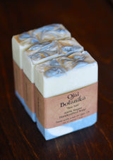 Three handcrafted Sea Salt Ojai Botanika Soap bars with marbled white and gray tops are arranged side by side on a dark wooden surface—luxurious, 100% vegan, cruelty-free skincare for everyone.