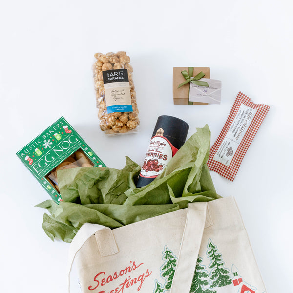 Holiday gift tote with eggnog cookies, chocolate cherries, and other items laid flat on a white background