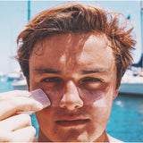 Man applying SIN-MIN Shade sunscreen on his face with a blue background