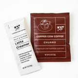A white Latte Creamer packet and a brown Single-Serve Pour Over Churro Coffee packet are side by side on a white background, highlighting the convenience of single-serve Vietnamese coffee.