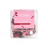 A clear box of Valentine’s Day Strawberry Cheesecake Chocolate Bark, pure Belgian chocolate with heart-shaped sprinkles. The pink label says "happy valentine’s day" with red hearts. Net wt: 2.5 oz (71 g).