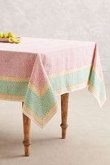 A rectangular table with Sunrise Fair Trade Block Printed Linen in pink, green, and yellow, topped with green apples.