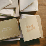 Stacks of embossed Happy Birthday Note Card greeting cards arranged on a wooden surface.