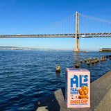 Box of Chewy Oat Cranberry Cookies sits by water with a large bridge visible in the background.