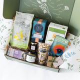 Gift basket with various products including a box of tea and a jar of honey, on a decorative surface.