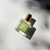 Sunday Olive Perfume Oil in a square glass bottle with a gold cap casts a shadow on white in bright sunlight.