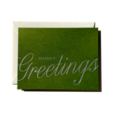 Season’s Greetings Note Card in green with silver foil text resting on a natural envelope.