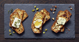 Three Pumpkin Spice Artisan Crisp toasts topped with cheese, honey, herbs & pumpkin seeds on a slate board.