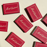 Several scarlet red Matchbox Merry Christmas boxes with gold text scattered on a light surface.