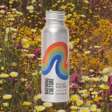 A Travel Size Mind and Body Wash stands among yellow and white wildflowers in a sunny field.
