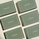 Six green rectangular Matchbox Cheers party favors arranged in a grid, each printed with a scalloped border.