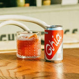 A can of Ghia Non-Alcoholic Spritz and a chilled glass with ice and orange slice on a wooden table.