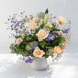 The Champagne + Flowers set features peach roses, purple and white blooms, and greenery in a white vase.