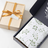 The Stolpman Wine & Snacks Gift Box sits beside artisan snacks in leafy-patterned paper and a gold-ribboned wood box.