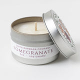 Pomegranate Travel Candle in a small tin with lid slightly open, showing the white soy wax inside.